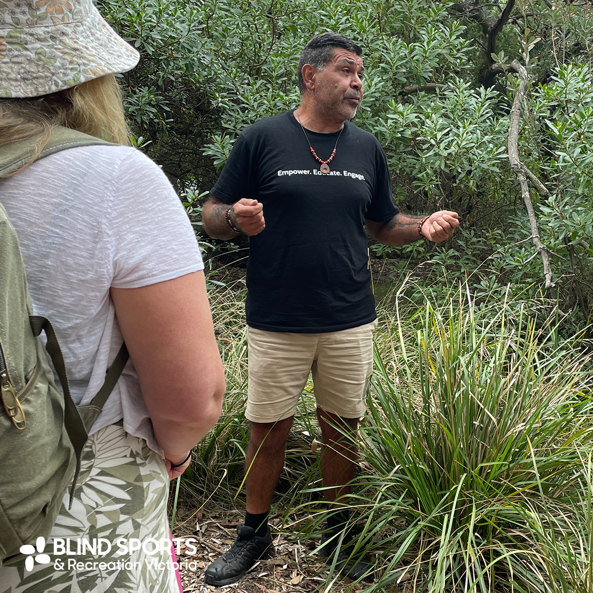 Lionel the indigenous culture guide standing in the bushland educating the participants about the surrounding plants and flowers.